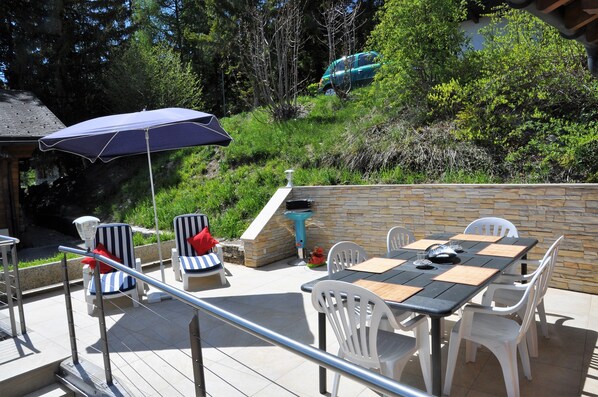 An outdoor patio with a table and chairs, a barbecue grill, and a stone wall.