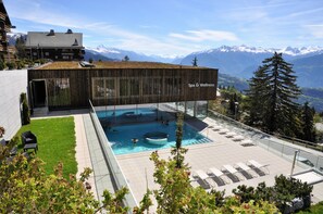 Ein modernes Gebäude mit Spa- und Wellnessbereich, Schwimmbad und Blick auf schneebedeckte Berge.