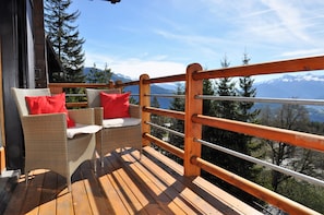 A wooden deck with wicker furniture and red cushions, overlooking a mountainous landscape. - Spacious chalet with a balcony and terrace offering panoramic views of the Rhône Valley   (Ayent)