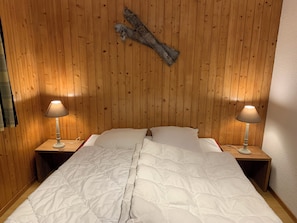 A room with a wooden paneled wall, a bed with white bedding, and two bedside lamps on wooden nightstands. - Spacious chalet with a balcony and terrace offering panoramic views of the Rhône Valley   (Ayent)