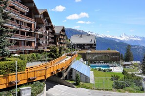 A modern building with balconies, a pool, and a mountain backdrop.