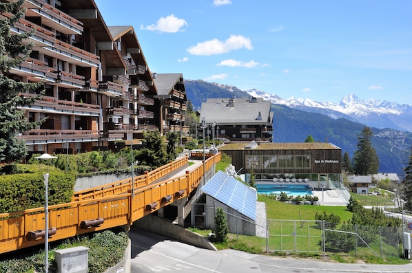 A modern building with balconies, a pool, and a mountain backdrop.