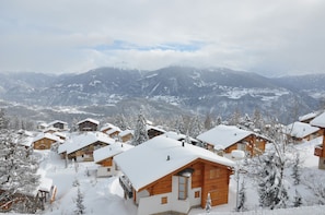 A cluster of wooden cabins with snow-covered roofs, set against a backdrop of snow-capped mountains. - Spacious chalet with a balcony and terrace offering panoramic views of the Rhône Valley   (Ayent)