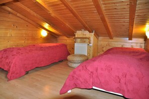 A cabin with two beds covered in red bedding, wooden walls, and a sloped ceiling with exposed beams.
