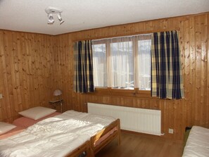Ein Zimmer mit Holzwänden, einem fenster mit Vorhängen, einem Bett und einer Heizung.