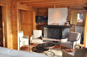 A log cabin interior with a stone fireplace, two armchairs, a sofa, and a television mounted on the wall. - Spacious chalet with a balcony and terrace offering panoramic views of the Rhône Valley   (Ayent)