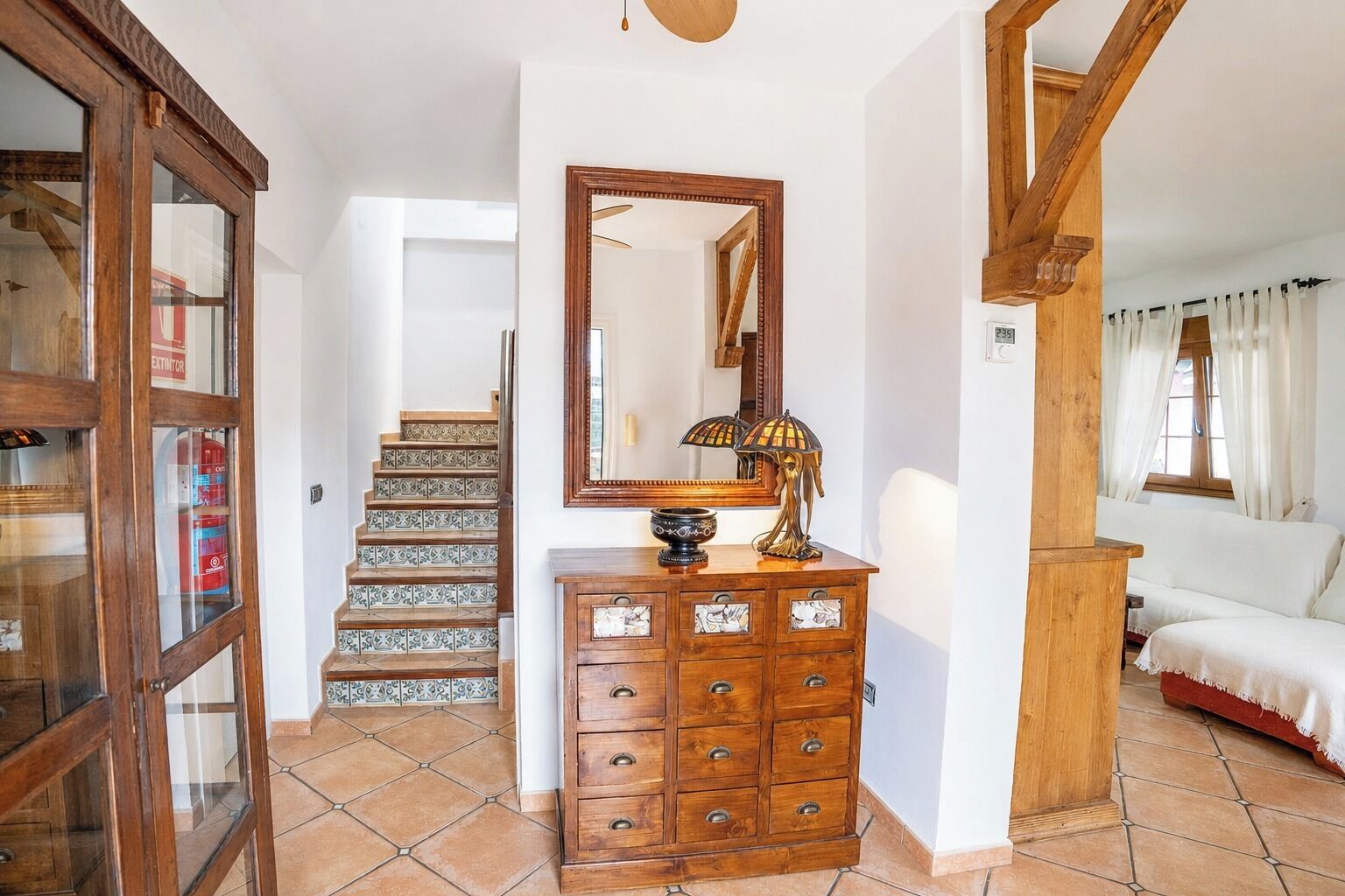A hallway with a wooden staircase, a wooden dresser with drawers, a mirror, and a lamp.