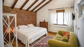 Een slaapkamer met een bed, een houten dressoir, een groene bank, een kamerkleed met dessin en een bakstenen muur.