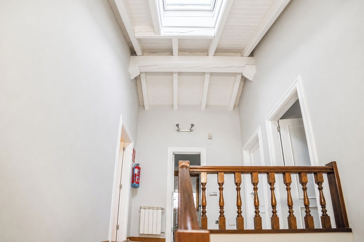 A staircase with a wooden handrail leading to a landing with a skylight.