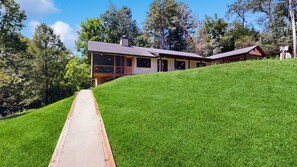A modern house with a large deck, surrounded by a well-maintained lawn and trees. - Cozy Creekside Retreat with Screened Porch & Outdoor Grill (Otto)