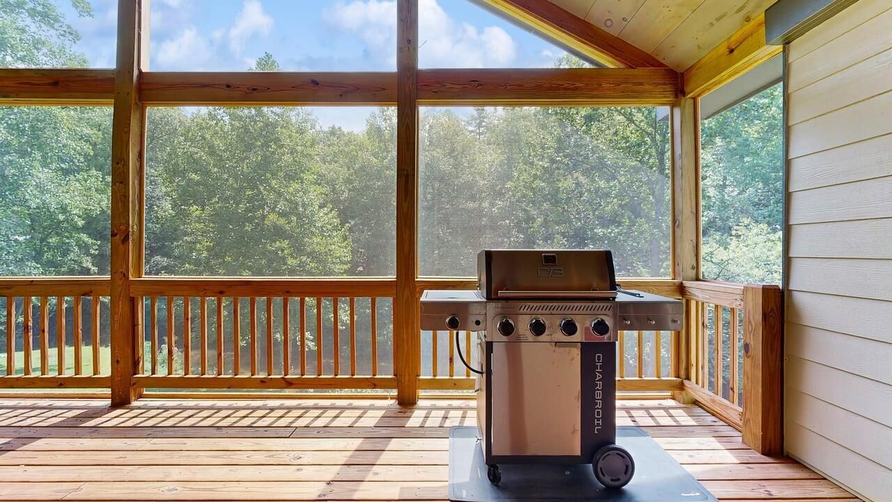 Ein überdachter Außenbereich mit Grill und Blick auf einen Wald.