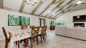 A dining area with a table and chairs, a sofa, a fireplace, and a TV mounted on the wall. - Cozy Creekside Retreat with Screened Porch & Outdoor Grill (Otto)