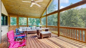 A covered deck with a ceiling fan, wicker furniture, and a view of trees. - Cozy Creekside Retreat with Screened Porch & Outdoor Grill (Otto)