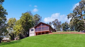 Una casa de dos pisos con un amplio ventanal en el nivel superior, rodeada de un césped y árboles.