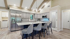 A modern kitchen with a central island, stainless steel appliances, and bar stools. - Cozy Creekside Retreat with Screened Porch & Outdoor Grill (Otto)