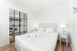 A modern hotel room with a large bed, two bedside tables with lamps, a wardrobe, and a visible laundry area. - GuestReady - Cosy Apartment in Freixo (Porto)