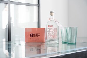 A glass table with a bottle of water, two glasses, and a pink box with the text 'GUEST READY' and 'Embrace your stay'. - GuestReady - Cosy Apartment in Freixo (Porto)