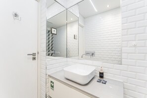 Uma casa de banho moderna com lavatório branco, espelho e área de duche.