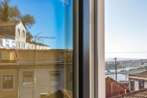 A view through a window with a building featuring a distinct architectural style, including a pointed roof and a visible window. - GuestReady - Cosy Apartment in Freixo (Porto)