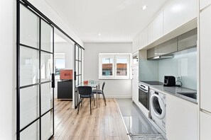 A modern kitchen with a washing machine, a coffee maker, and a dining area with chairs and a table. - GuestReady - Cosy Apartment in Freixo (Porto)