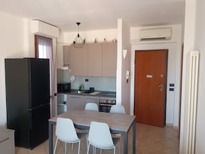 Een kleine keuken met een koelkast, magnetron, spoelbak en een eethoek met stoelen.