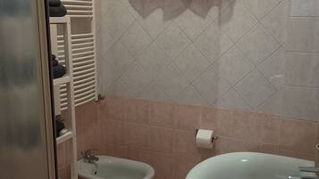 Un baño con un bidé, un lavamanos, un perchero para toallas y una ventana con cortina.