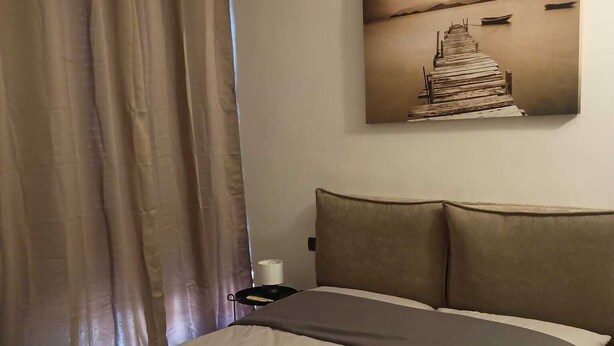 Et hotelværelse med seng, gardiner, et natbord, en lampe og et billede på væggen.