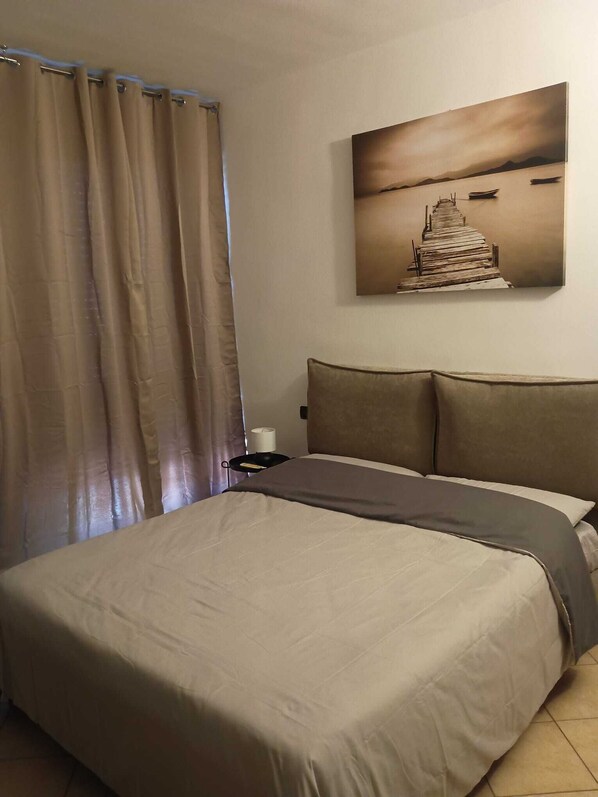 Een hotelkamer met een bed, gordijnen, een nachtkastje, een lamp en een aan de muur hangend schilderij.
