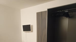 Et moderne soveværelse med en seng, et fjernsyn monteret på væggen, et klædeskab og et lille bord med en lampe.