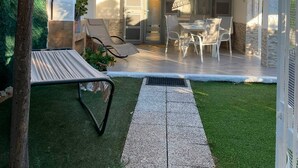 Un patio techado al aire libre con zona de estar, un árbol y un sendero que lleva a la entrada.