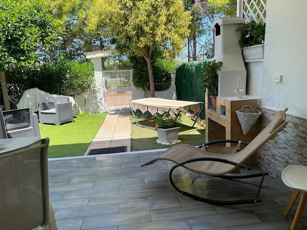 A patio with a lounge chair, a small table, and a grill area.