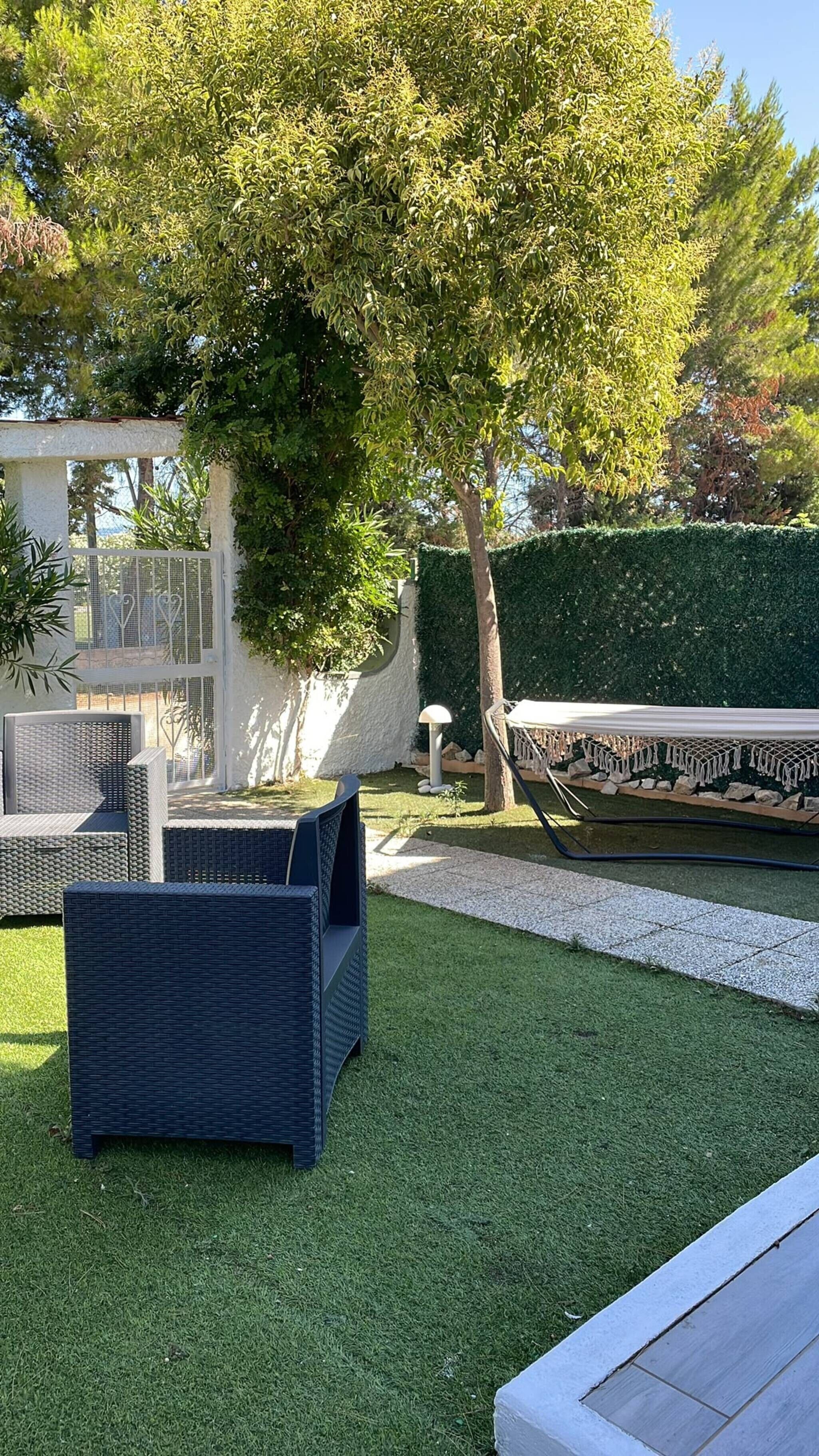 Un'area patio con mobili da esterno, un siepe e un muro bianco.