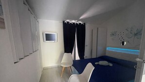 Un dormitorio con una cama, un escritorio, una silla, un televisor pequeño y un adorno de pared.