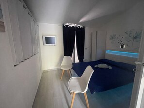 Ein Schlafzimmer mit einem Bett, einem Schreibtisch, einem Sessel, einem kleinen Fernseher und einer Wanddekoration.