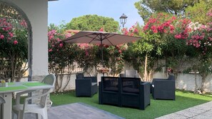 Eine Terrasse im Freien mit Tisch und Stühlen, umgeben von üppigem Grün und blühenden Pflanzen.
