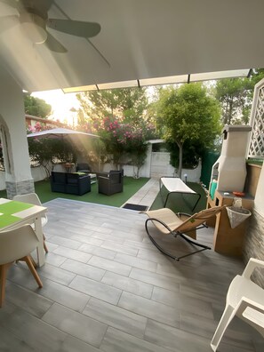 A covered patio area with a table, chairs, a grill, and a view of the garden.