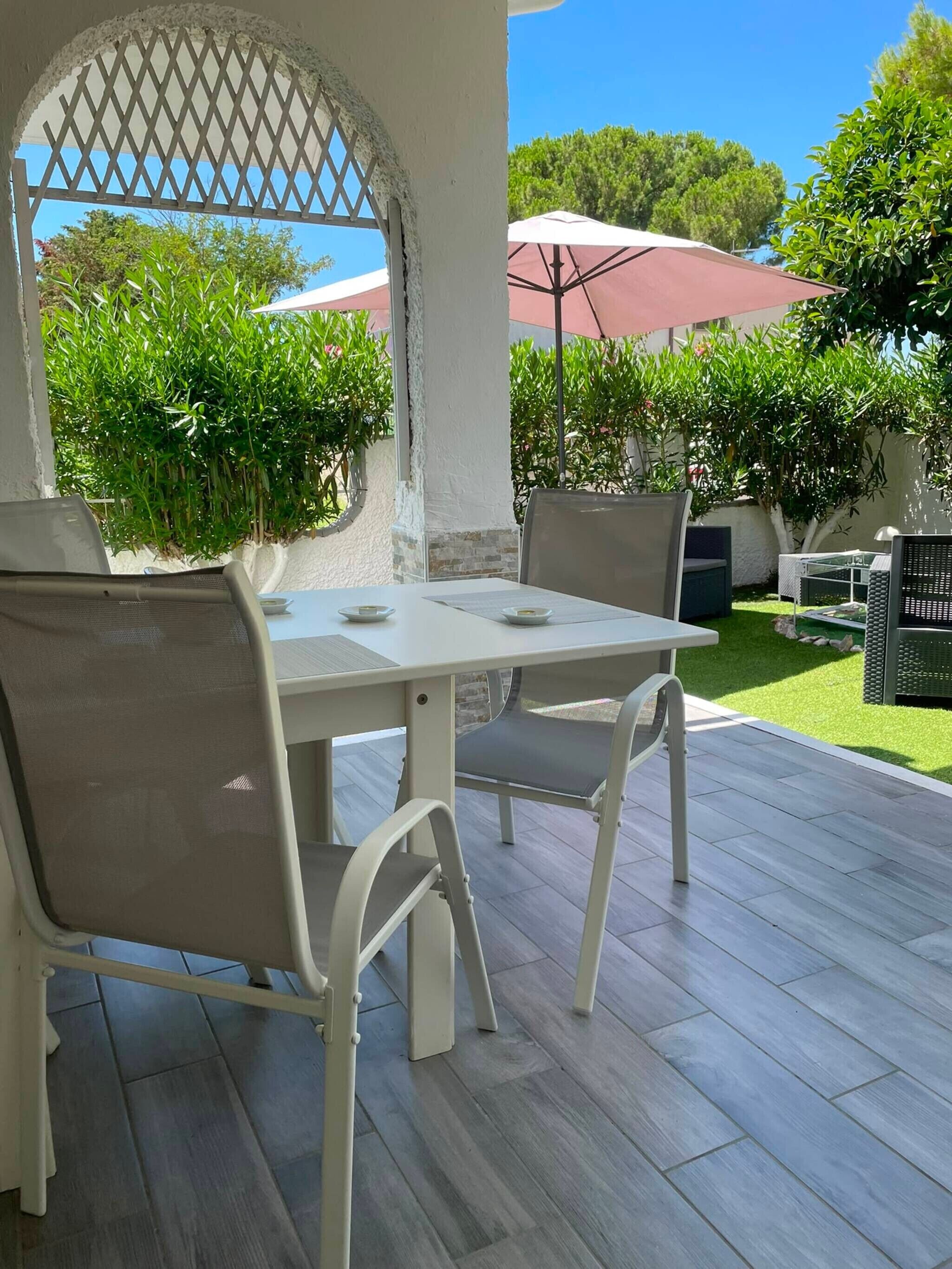 Eine Terrasse im Freien mit Tisch und Stühlen, umgeben von viel Grün und einem wolkenlosen Himmel.