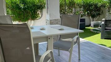 Eine Terrasse im Freien mit Tisch und Stühlen, umgeben von viel Grün und einem wolkenlosen Himmel.