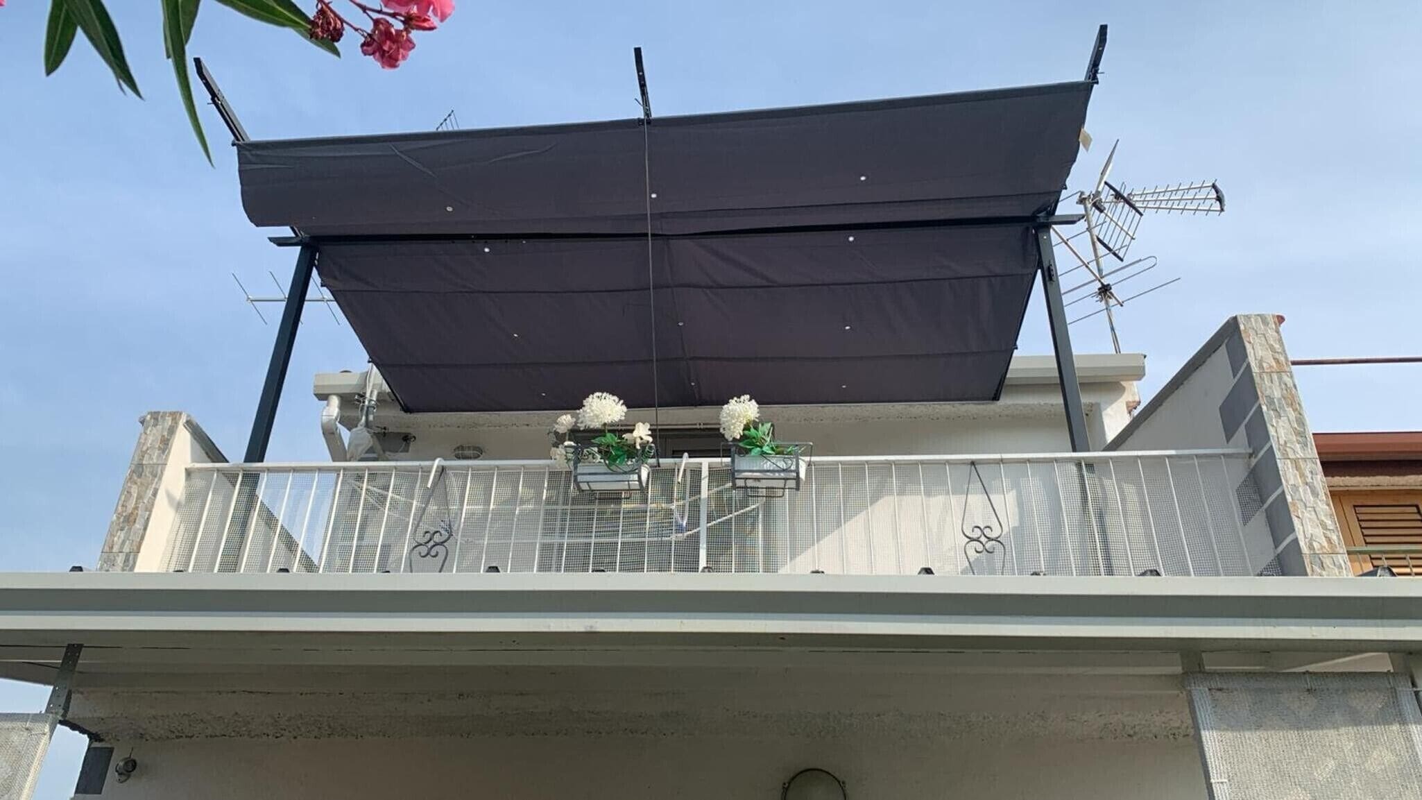 Un balcon doté d’une rambarde en métal, d’un auvent noir et de deux jardinières contenant des fleurs blanches.