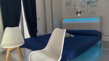 Une chambre à coucher avec un lit, deux chaises, une table de chevet et un mur orné d’un motif floral.