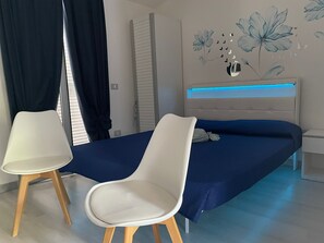 A bedroom with a bed, two chairs, a nightstand, and a wall with a floral design.