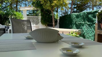 Un espace de restauration en plein air avec une table dressée pour deux personnes, entouré de verdure et d’arbres.