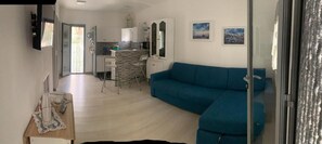 A living room with a blue sofa, a kitchen area with a counter and cabinets, and a dining table with chairs.