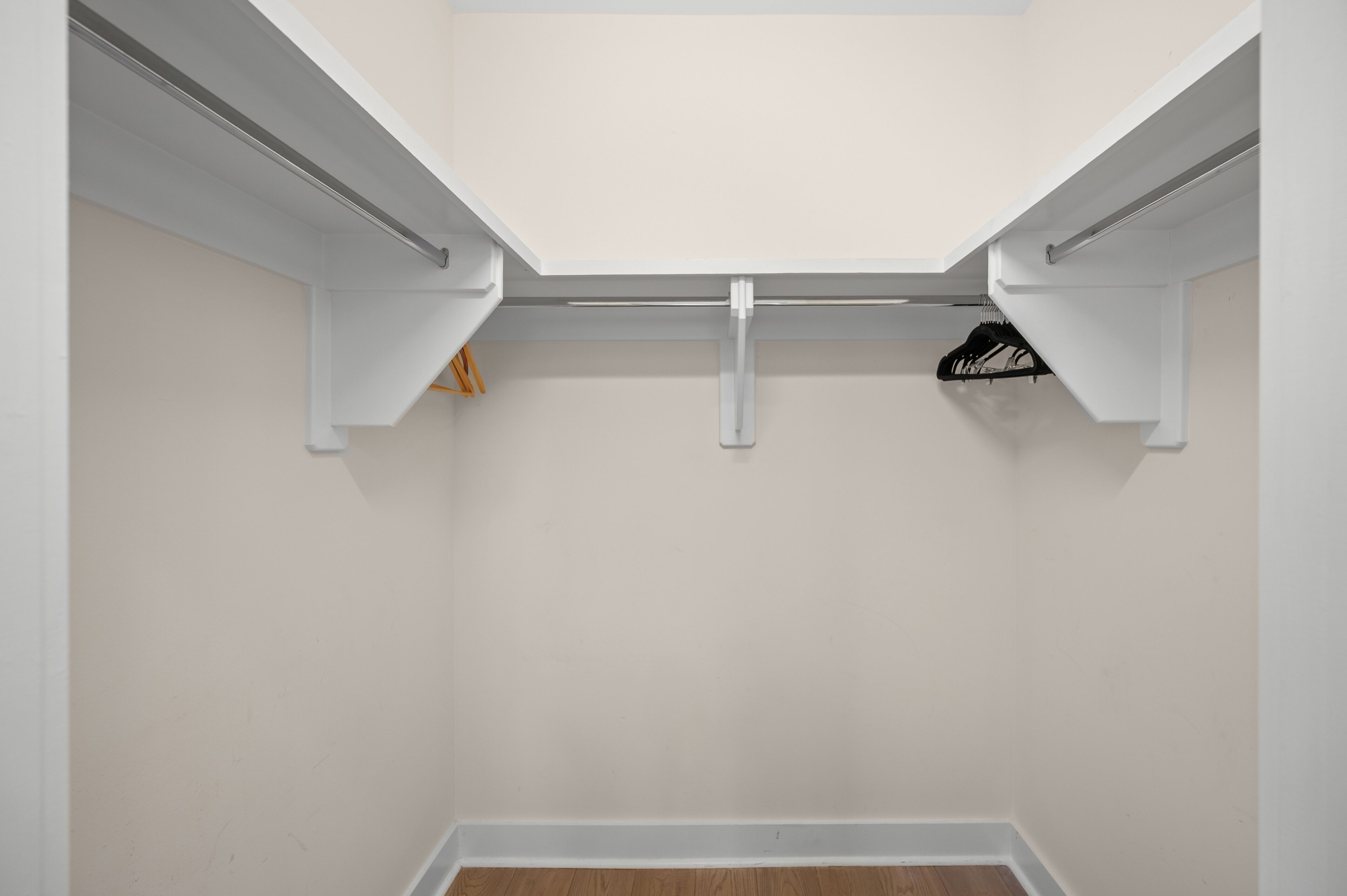 A closet with white walls and a wooden floor, featuring a metal rod for hanging clothes.