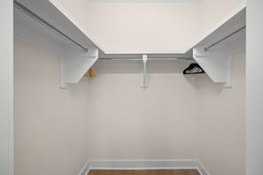Un armario con paredes blancas y suelo de madera, que incluye una barra metálica para colgar ropa.
