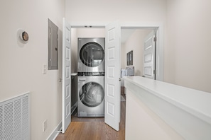 Une buanderie équipée de deux machines à laver et deux sèche-linge à chargement frontal superposés, une porte blanche et un mur blanc.