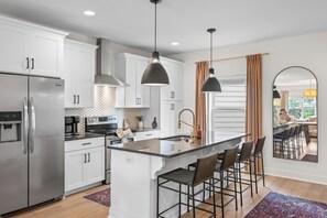 A modern kitchen with stainless steel appliances, white cabinetry, and a central island with bar stools. - Luxurious Townhome in the Nations w/ Penthouse style top floor & walkout balcony (Nashville)