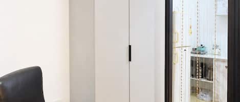 Una habitación con una silla de cuero negro, un armario blanco y una cocina visible a través de un vano.