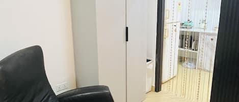 A room with a black leather chair, a white wardrobe, a tiled floor, and a view through a partially open door.