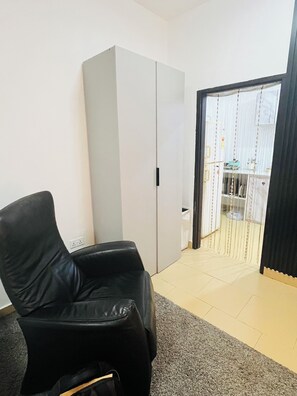 Una habitación con una butaca de cuero negro, un armario blanco, suelo de baldosas y vistas por una puerta entreabierta.